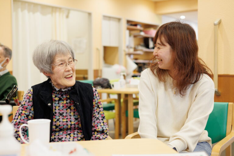 介護施設内で高齢者と職員がテーブルで会話・交流している風景